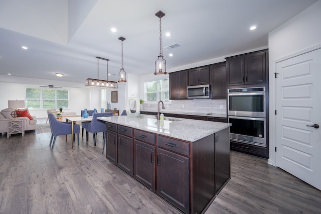 kitchen with pendant lighting, stainless steel appliances, a healthy amount of sunlight, and an island with sink