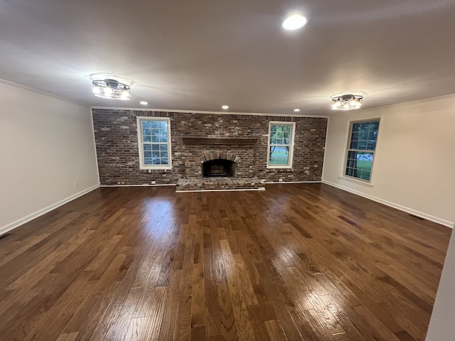 unfurnished living room with brick wall, a large fireplace, crown molding, and dark hardwood / wood-style floors