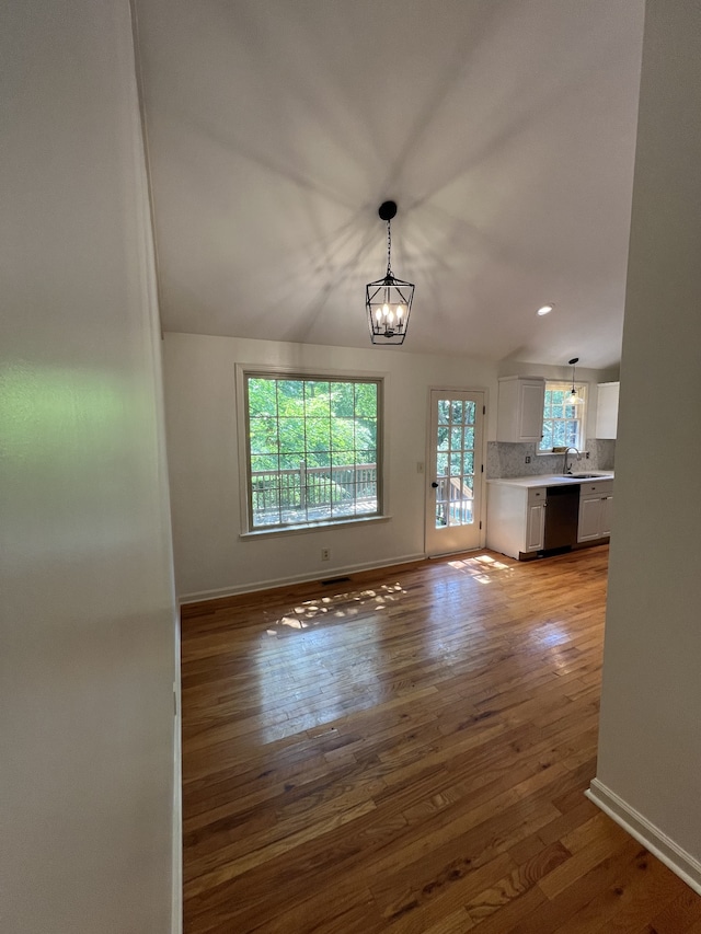 unfurnished living room featuring wood-type flooring, vaulted ceiling, sink, and an inviting chandelier