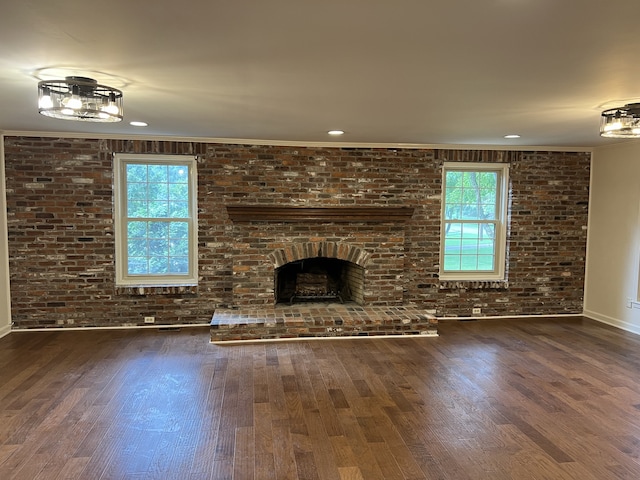 unfurnished living room with dark wood-type flooring, a brick fireplace, brick wall, and a wealth of natural light