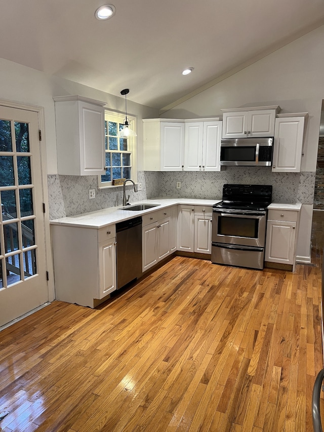 kitchen with lofted ceiling, light wood-type flooring, stainless steel appliances, hanging light fixtures, and sink