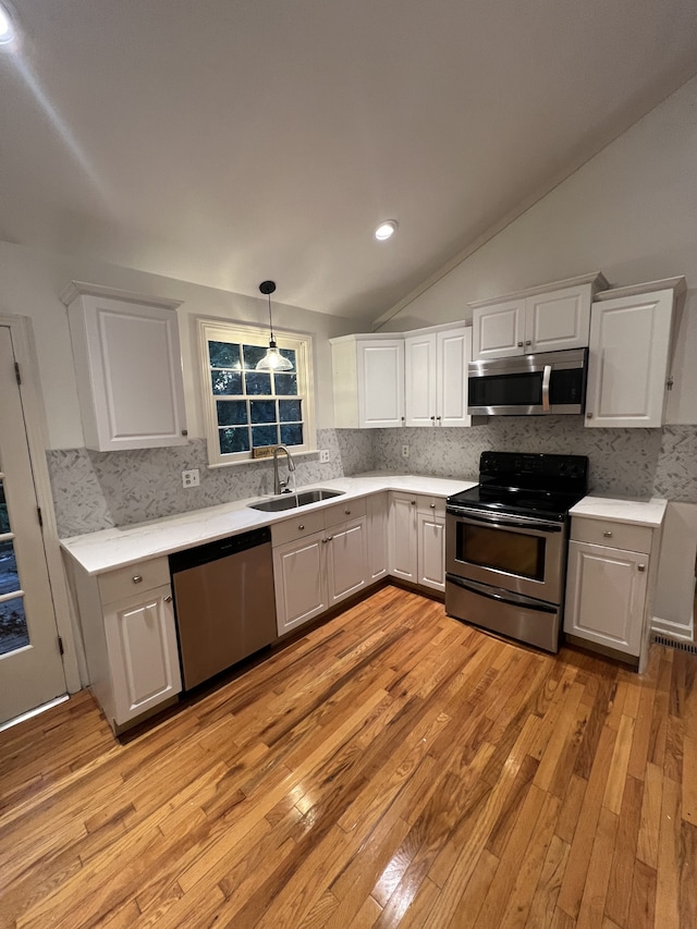 kitchen with stainless steel appliances, white cabinets, light wood-type flooring, sink, and lofted ceiling