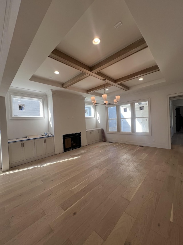 unfurnished living room with plenty of natural light, beam ceiling, light wood-type flooring, and a chandelier