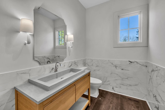 bathroom featuring wood-type flooring, tile walls, vanity, and toilet