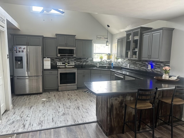 kitchen with dark countertops, pendant lighting, stainless steel appliances, and glass insert cabinets