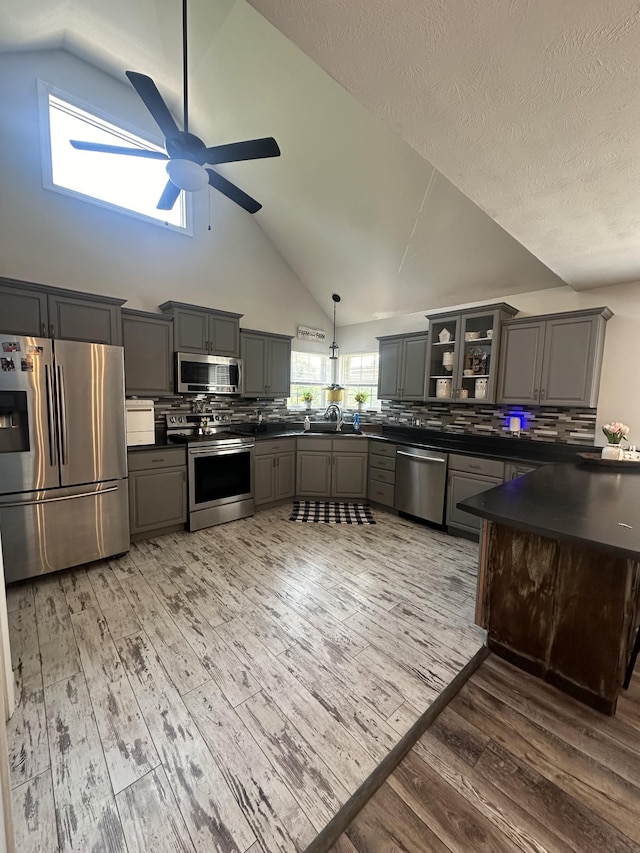 kitchen with dark countertops, appliances with stainless steel finishes, glass insert cabinets, hanging light fixtures, and gray cabinets