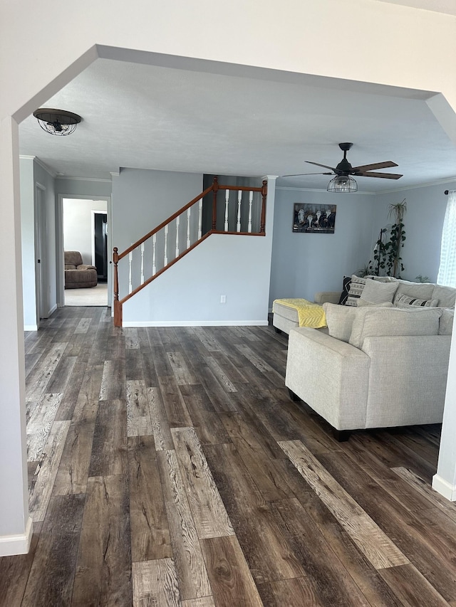 unfurnished living room with ceiling fan, dark wood-type flooring, baseboards, ornamental molding, and stairway