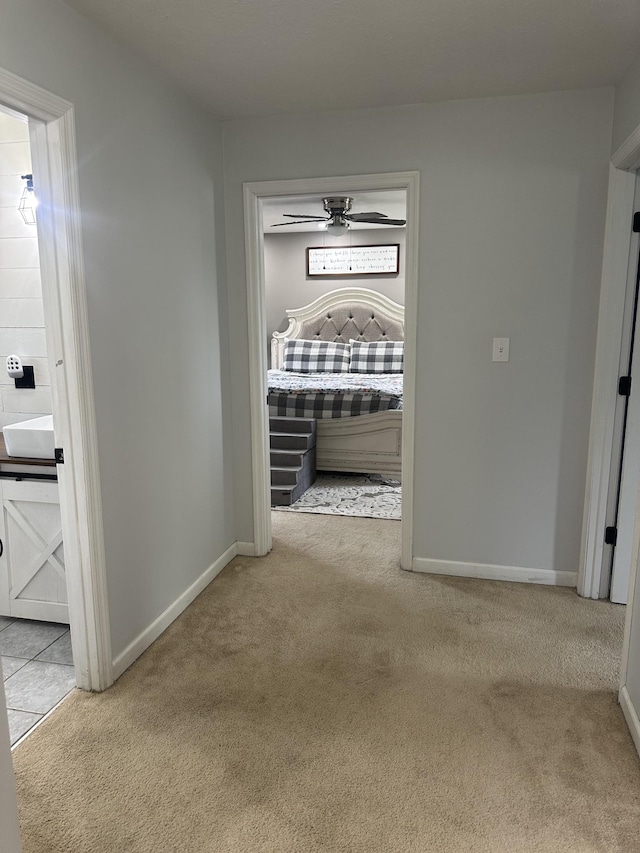 corridor with baseboards and light colored carpet