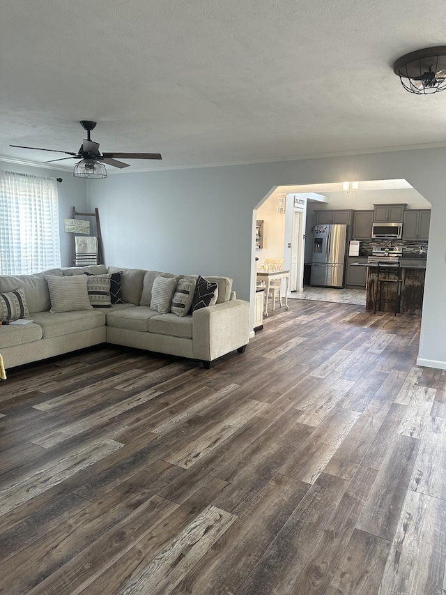 unfurnished living room featuring dark wood-style floors, a textured ceiling, arched walkways, and a ceiling fan