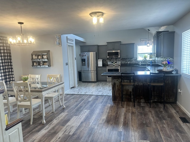 kitchen with decorative light fixtures, dark countertops, appliances with stainless steel finishes, a sink, and a kitchen breakfast bar