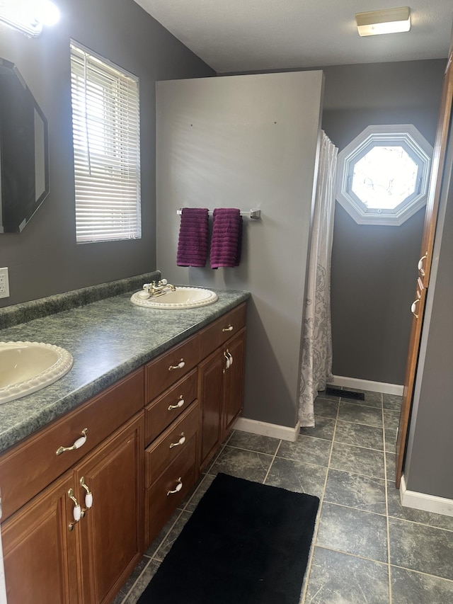 full bath with a sink, baseboards, and double vanity