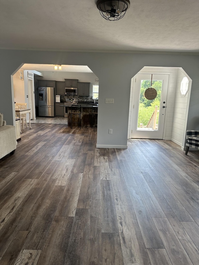 entrance foyer with arched walkways, dark wood-type flooring, ornamental molding, and baseboards