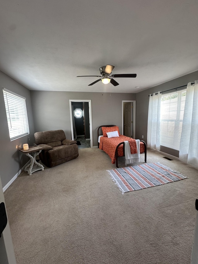 carpeted bedroom featuring baseboards, multiple windows, visible vents, and a ceiling fan