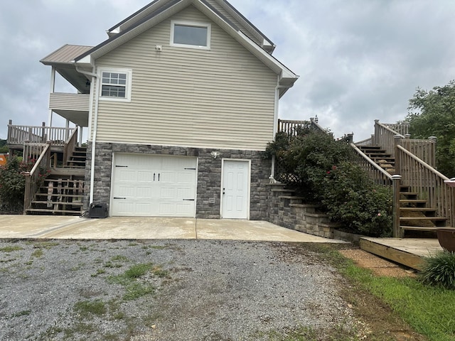 rear view of property with metal roof, an attached garage, stairs, driveway, and stone siding