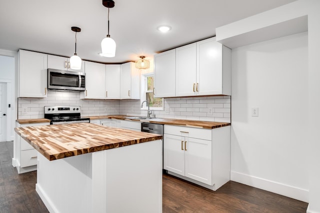 kitchen with pendant lighting, stainless steel appliances, a center island, white cabinets, and wood counters