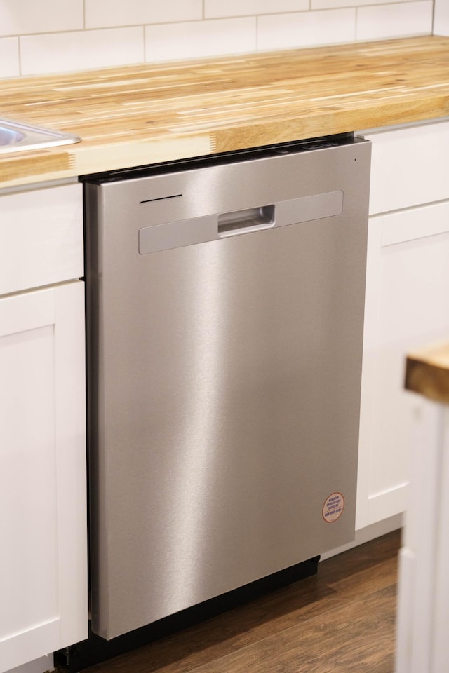 details with tasteful backsplash, white cabinetry, stainless steel dishwasher, and dark hardwood / wood-style flooring