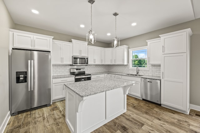 kitchen with appliances with stainless steel finishes, white cabinets, wood-type flooring, a center island, and sink