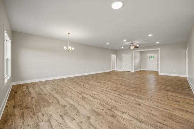 unfurnished living room with ceiling fan with notable chandelier and light hardwood / wood-style floors