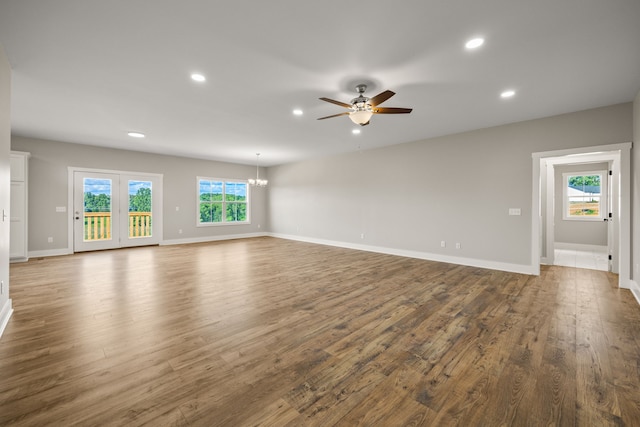 unfurnished living room featuring ceiling fan with notable chandelier, a wealth of natural light, and dark wood-type flooring