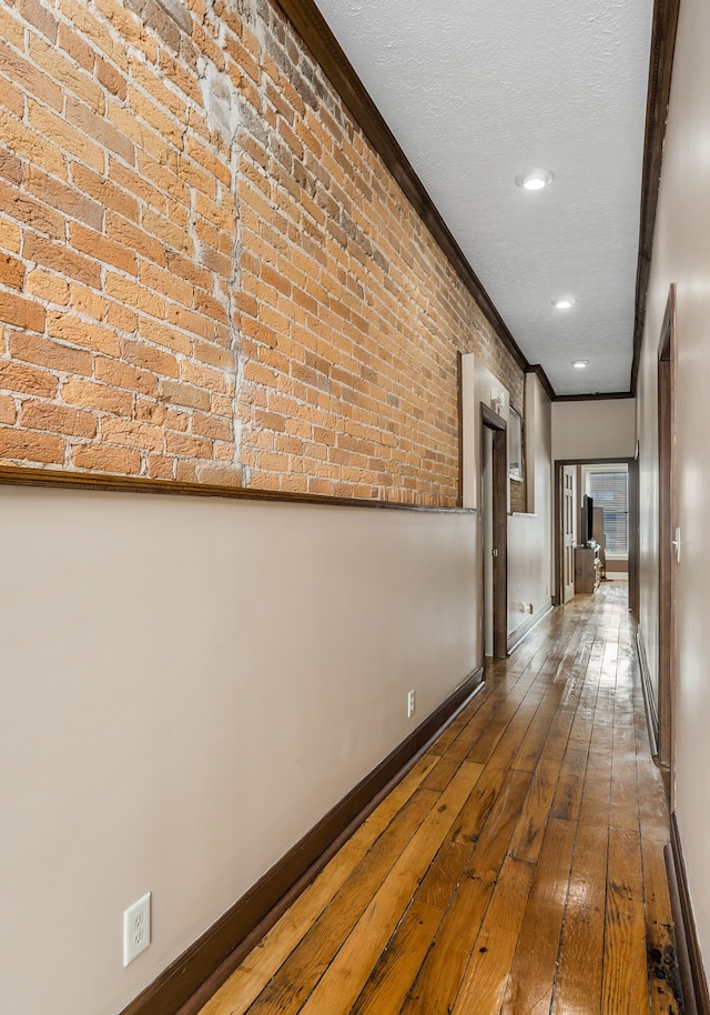 hallway with brick wall, ornamental molding, a textured ceiling, and hardwood / wood-style flooring