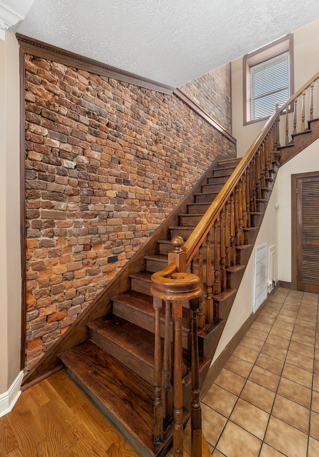 stairway featuring brick wall, a textured ceiling, and light hardwood / wood-style floors