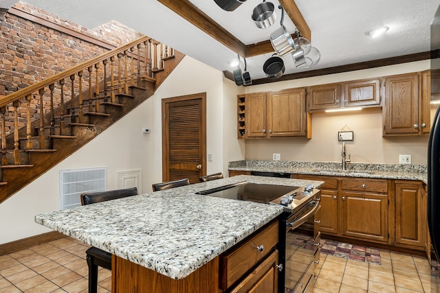 kitchen with sink, range with electric stovetop, light stone countertops, a kitchen island, and light tile patterned floors