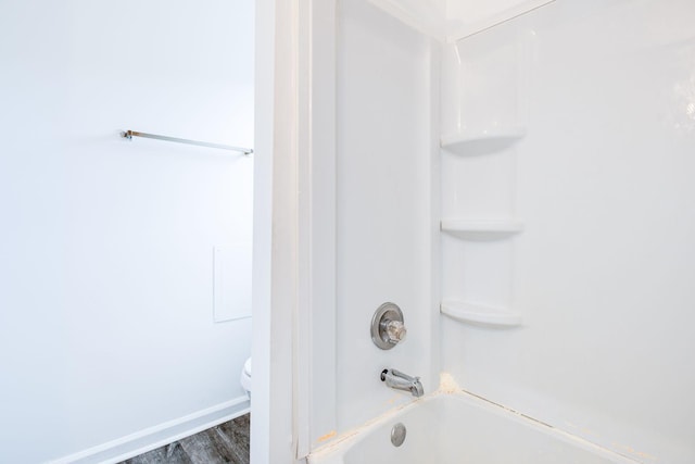 bathroom featuring toilet, baseboards, tub / shower combination, and wood finished floors