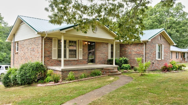 single story home featuring covered porch, a front yard, metal roof, and brick siding