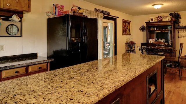 kitchen featuring light stone counters, black fridge, and dark wood finished floors