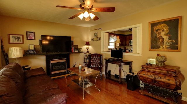 living area featuring a ceiling fan, a glass covered fireplace, and wood finished floors