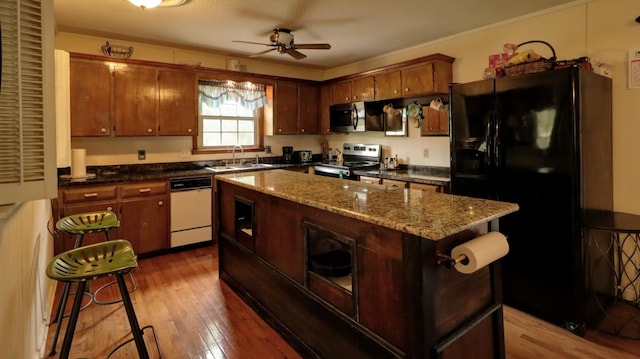 kitchen with a center island, appliances with stainless steel finishes, a ceiling fan, a sink, and wood finished floors