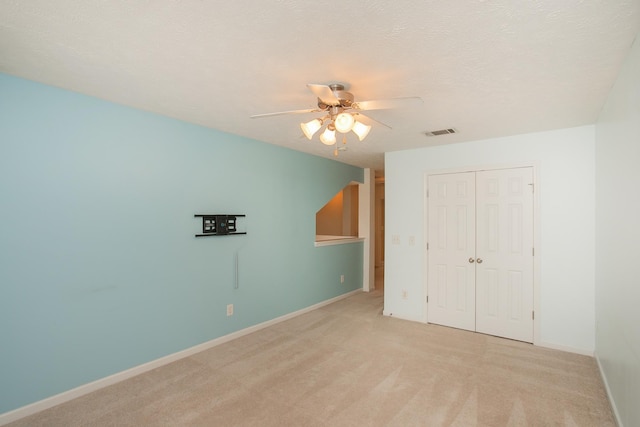 unfurnished bedroom with light carpet, a textured ceiling, a closet, and ceiling fan