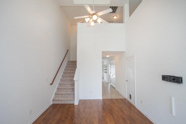 staircase with hardwood / wood-style floors, a high ceiling, and ceiling fan