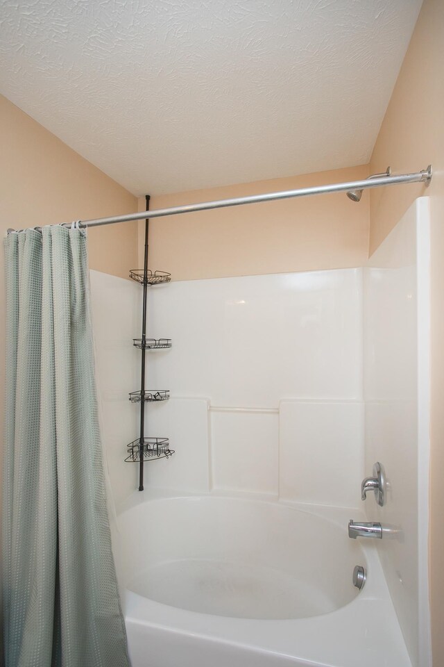 bathroom with shower / bathtub combination with curtain and a textured ceiling