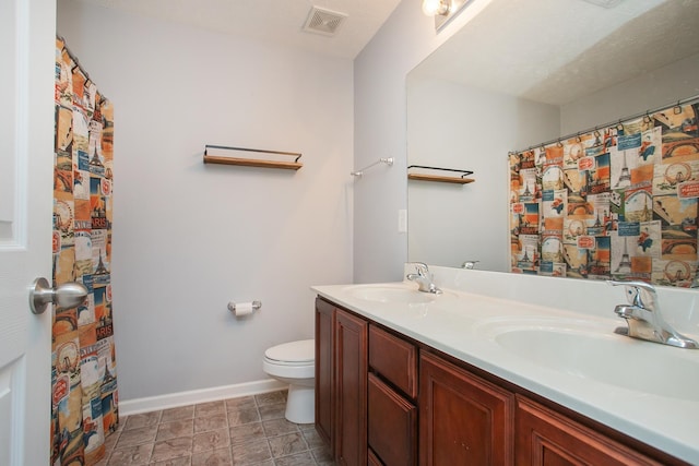 bathroom with a textured ceiling, toilet, dual bowl vanity, and tile patterned flooring