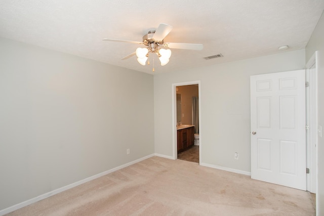 unfurnished bedroom featuring ensuite bath, light colored carpet, and ceiling fan