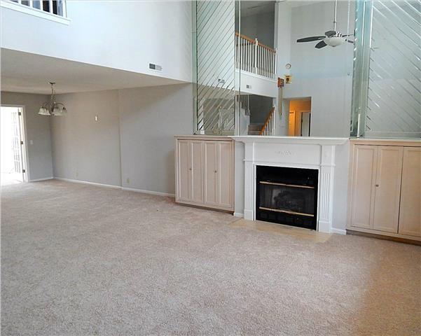 unfurnished living room featuring a glass covered fireplace, light colored carpet, a high ceiling, and ceiling fan with notable chandelier