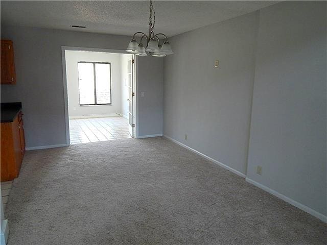 unfurnished dining area with visible vents, light colored carpet, an inviting chandelier, a textured ceiling, and baseboards