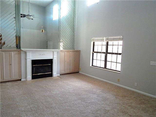 unfurnished living room with a fireplace with flush hearth, baseboards, light colored carpet, and a high ceiling