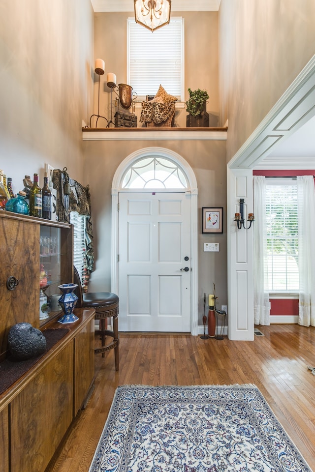 foyer entrance featuring hardwood / wood-style flooring, a towering ceiling, and crown molding