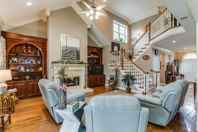 living room with crown molding, ceiling fan, light hardwood / wood-style floors, a tiled fireplace, and high vaulted ceiling