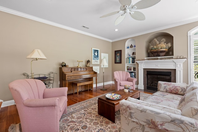 living room with built in shelves, ornamental molding, hardwood / wood-style floors, and ceiling fan