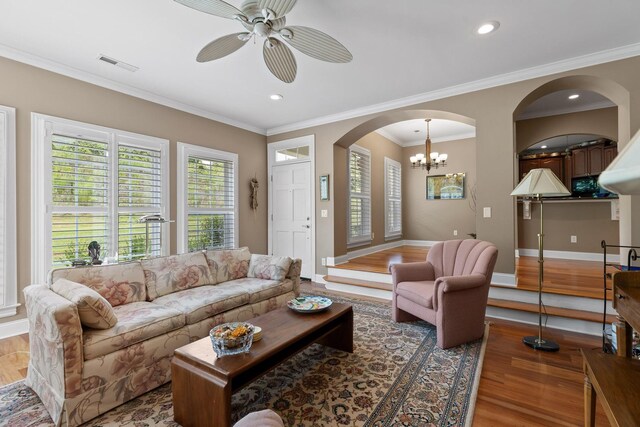 living room with ceiling fan with notable chandelier, wood-type flooring, and crown molding