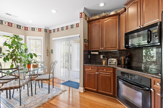 kitchen with dark stone counters, black appliances, light hardwood / wood-style floors, backsplash, and crown molding