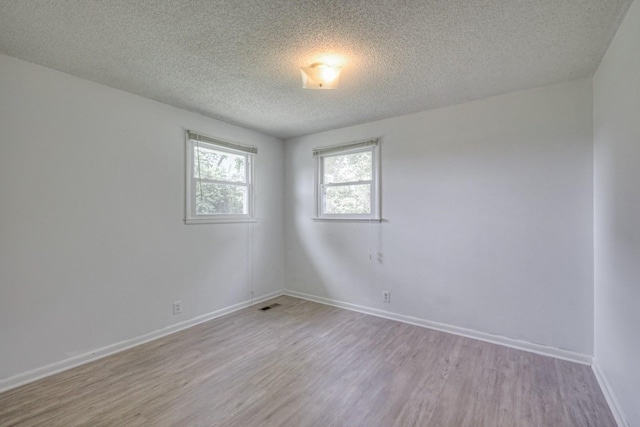 unfurnished room featuring light wood-style floors, baseboards, and a textured ceiling