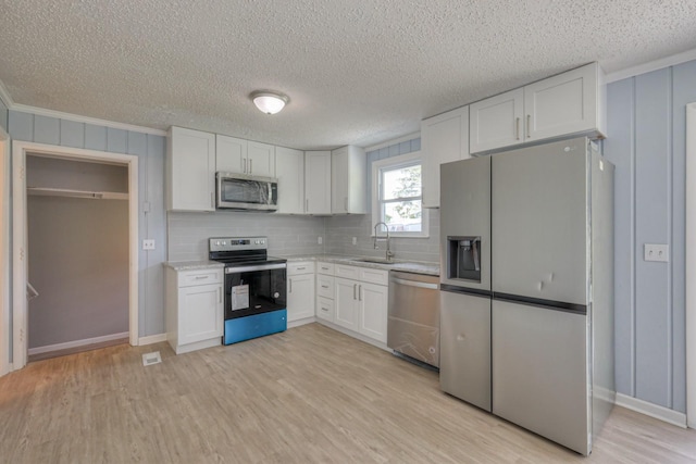 kitchen with a sink, white cabinetry, light countertops, appliances with stainless steel finishes, and light wood finished floors