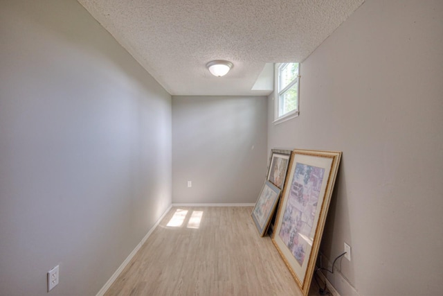 unfurnished room with light wood-style floors, a textured ceiling, and baseboards