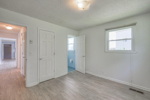 unfurnished bedroom with a textured ceiling, light wood-style flooring, visible vents, and baseboards