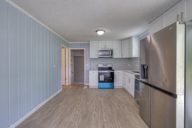 kitchen featuring light wood finished floors, light countertops, appliances with stainless steel finishes, ornamental molding, and white cabinets