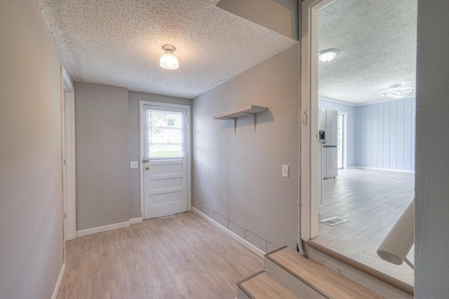 doorway with visible vents, a textured ceiling, baseboards, and wood finished floors